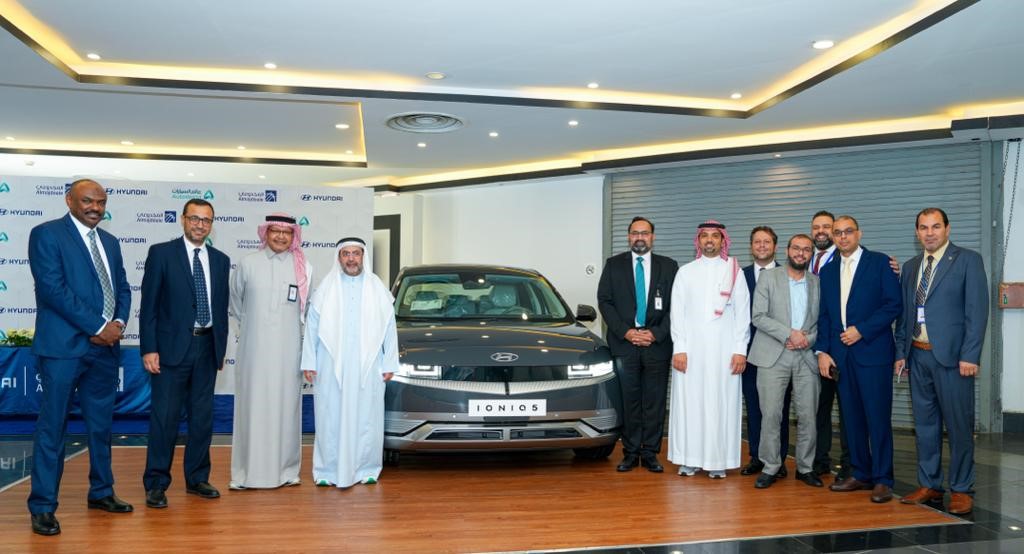 A group of men standing in front of a car

Description automatically generated